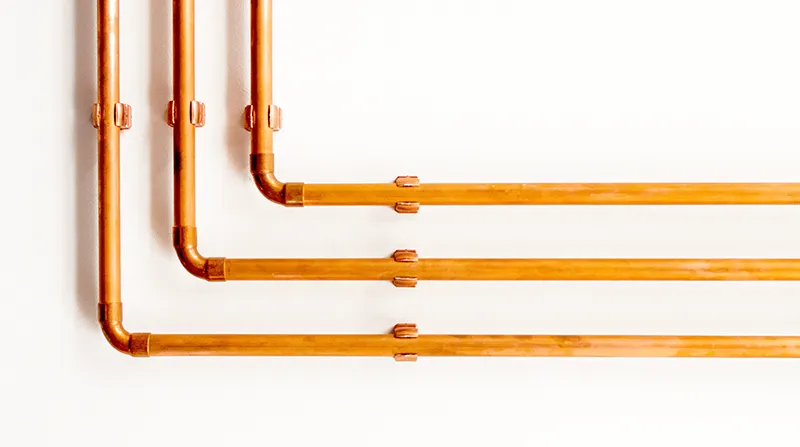Heizungs- und Kältetechnik. Bild: Kupferrohre an weißer Wand.